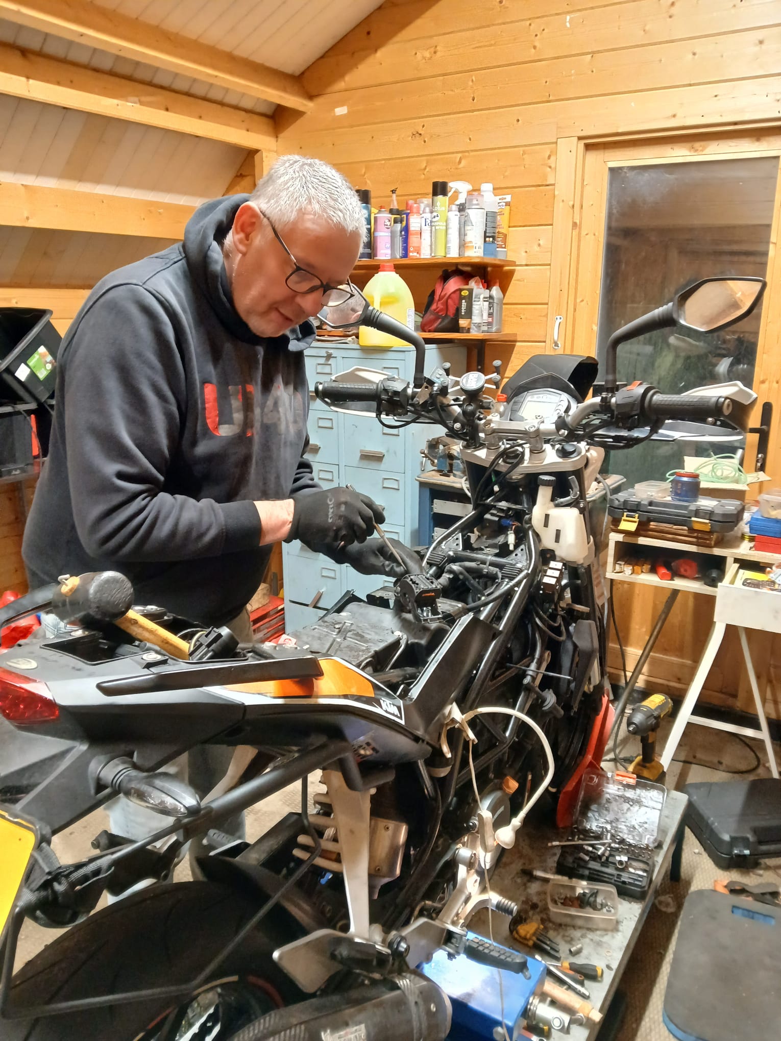 Onderhoud aan een KTM-motor in de houten werkplaats, met olies en spullen op de plank