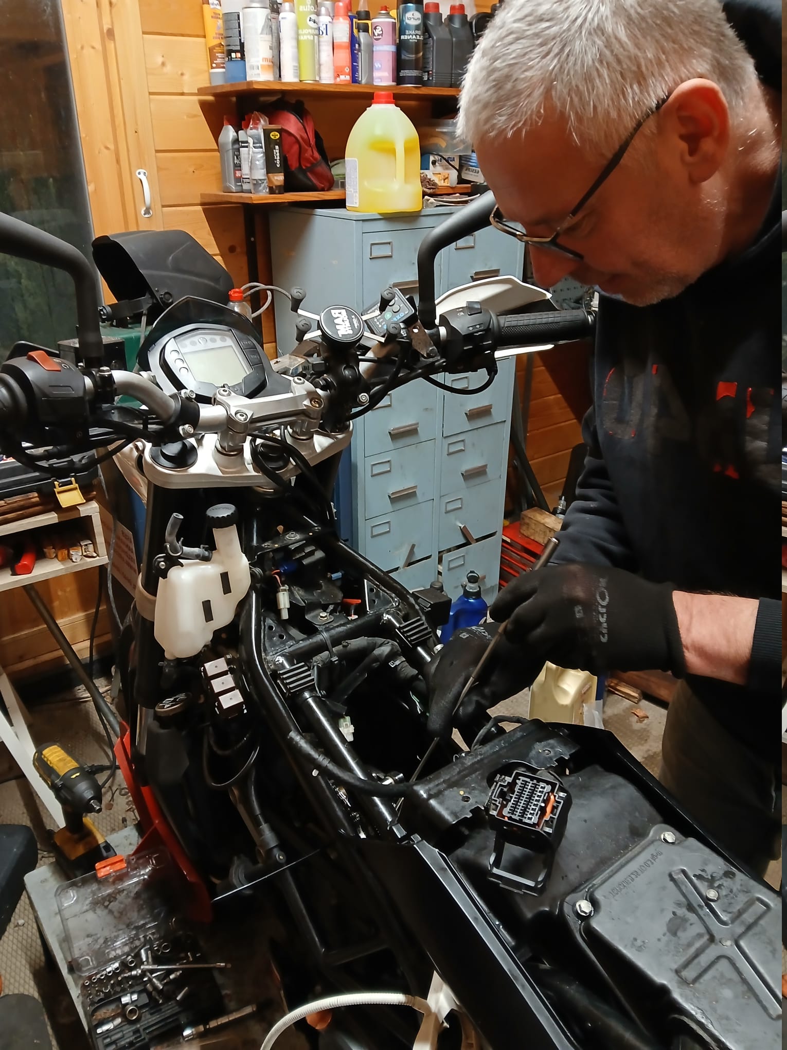 Onderhoud aan een KTM-motor in de houten werkplaats, met olies en spullen op de plank